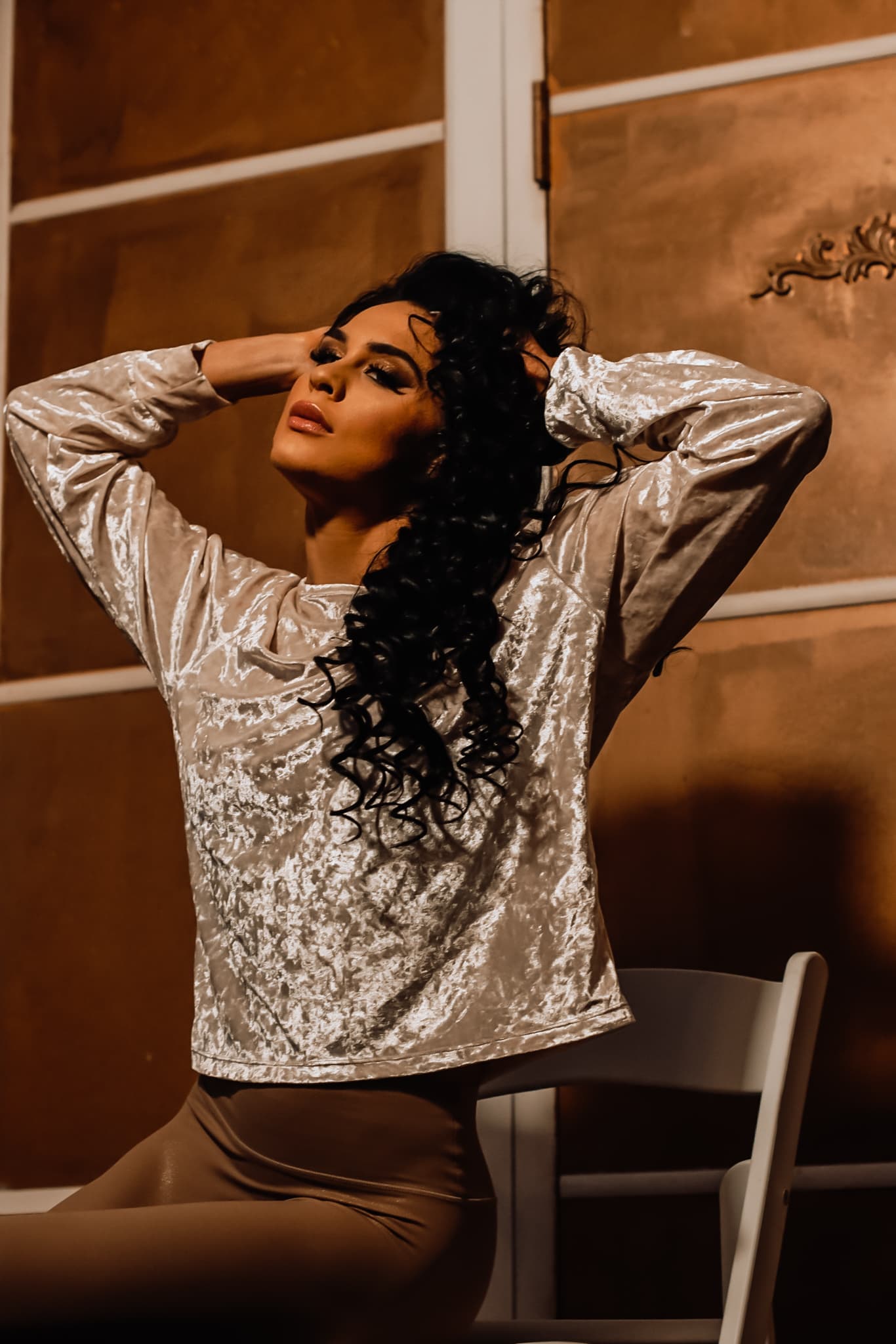 Glamorous woman with dark curls poses in a velvet top against a golden background.